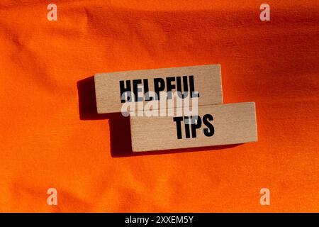 Helpful tips message written on wooden blocks with orange background. Conceptual helpful tips symbol. Copy space. Stock Photo