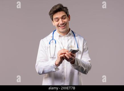 Rich doctor man counting money. Handsome medical health care worker in white coat with USD dollars banknotes. White studio background. High quality 4k Stock Photo