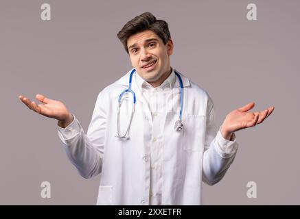 Confused 30s aged physician in white medical coat form, shoulders up - can't help, makes gesture of I dont know. Difficult question, guilty reaction, Stock Photo