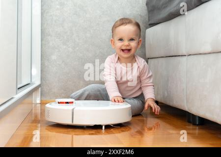 Laughing baby playing with robot vacuum cleaner. Robot friendship concept Stock Photo