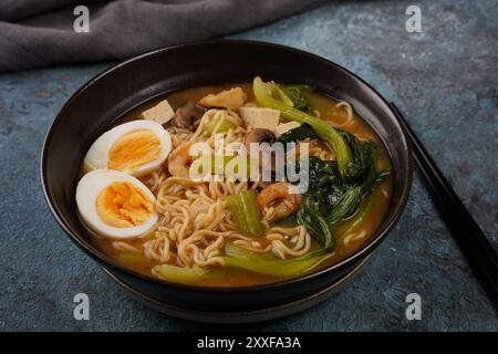 Asian  ramen noodle soup with shrimps, roasted tofu and  mushrooms in a bowl. Stock Photo