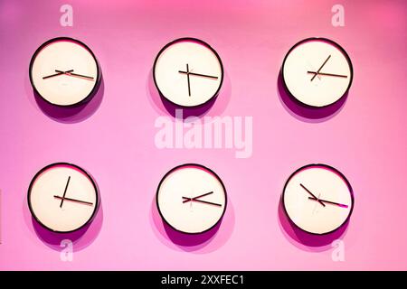 Six analog wall clocks displaying different times on a vibrant pink background. world time zone concept Stock Photo