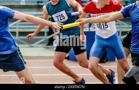 passing baton to men team athletes in athletics relay race Stock Photo