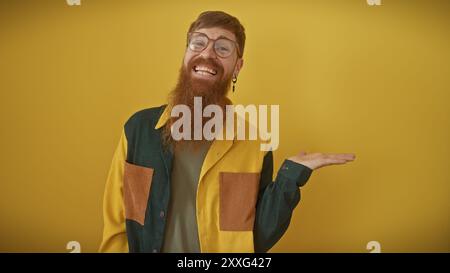 A smiling bearded redhead man in casual attire gesturing, isolated on a yellow background. Stock Photo