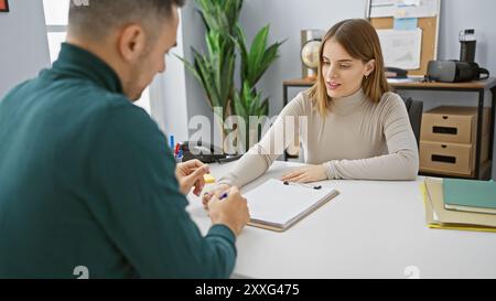 Woman and man coworkers collaborating in a modern office setup, discussing over documents on a desk. Stock Photo