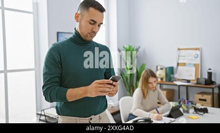 A focused man and a woman coworker engaging with technology in a modern office setting. Stock Photo