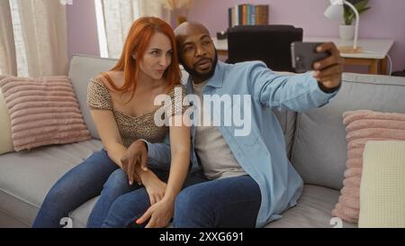 Couple taking a selfie in their living room, showcasing an interracial relationship with a loving atmosphere in their home as they sit together on a c Stock Photo