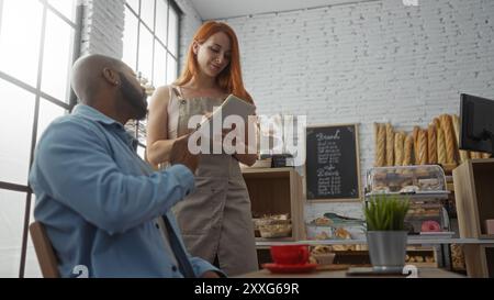 Woman waitress taking order from man customer in a bakery with shelves of bread in the background Stock Photo