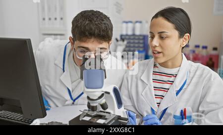 A man and woman in lab coats analyze samples using a microscope in a laboratory setting. Stock Photo