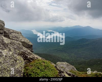 From the rocky summit of Whiteface Mountain, a dramatic view unfolds over Lake Placid, East Lake, and West Lake, shrouded in the mist of a grey sky Stock Photo