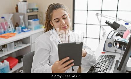 A young hispanic woman scientist analyzes data on a tablet in a laboratory setting, representing technology and healthcare. Stock Photo