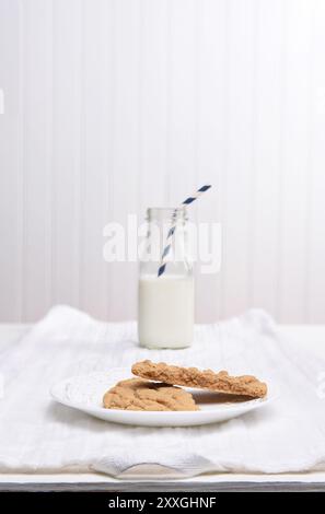 A plate of cookies on a white plate on a white kitchen towel, A bottle of milk in the background is intentionally out of focus. Stock Photo
