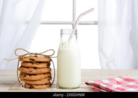 Horizontal shot of an after school snack of chocolate chip cookies and an old fashioned bottle of milk. The cookies are tied with twine and with a nap Stock Photo