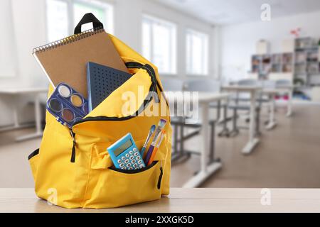 Yellow backpack with stationery on school desk in classroom. Space for text Stock Photo