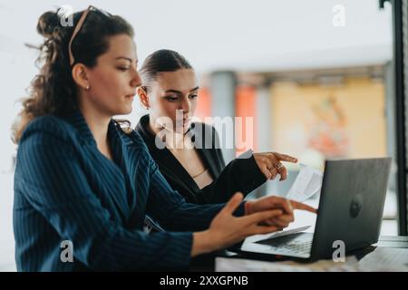 Two businesswomen collaborating on a project using a laptop in a modern office setting Stock Photo