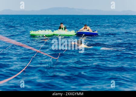 People enjoying summer tubing adventure on bright blue sea behind a speedboat Stock Photo