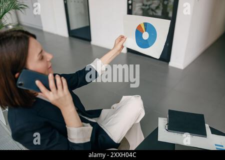 Businesswoman analyzing pie chart during phone meeting, focusing on efficiency and strategy Stock Photo