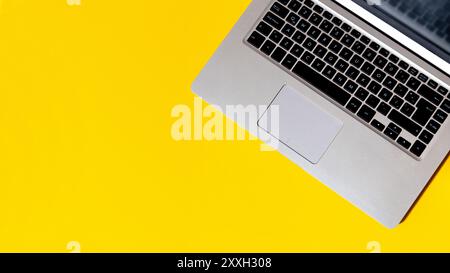 Top view of a grey laptop isolated over yellow background with copy space for you design. Flat lay photo with clear and minimalist composition. Stock Photo