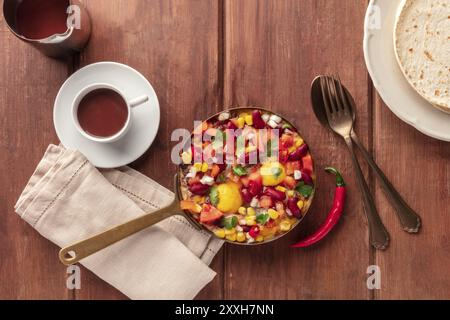 Mexican breakfast food. Huevos rancheros, the fried eggs, shot from the top with the pico de gallo salad, hot chocolate, and tortillas on a dark rusti Stock Photo