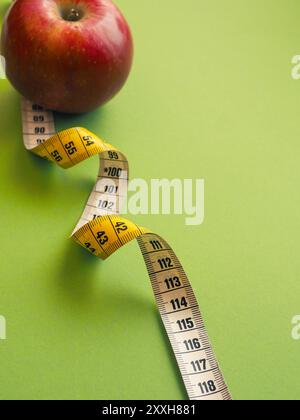 Diet or healthy eating concept with a measuring tape and an organic apple on a green background, space for text and selective focus on foreground Stock Photo