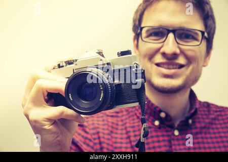 Young man in red-blue checked shirt is taking a picture with an vintage camera, retro style Stock Photo