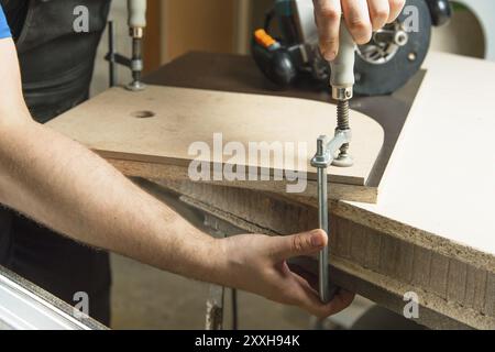 Close up Master clamps the workpiece with a dvp clamp to the workbench and on the background lies Carpentry hand router Stock Photo