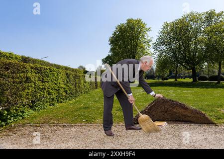 Business man sweeps something under the carpet, symbolic image Stock Photo