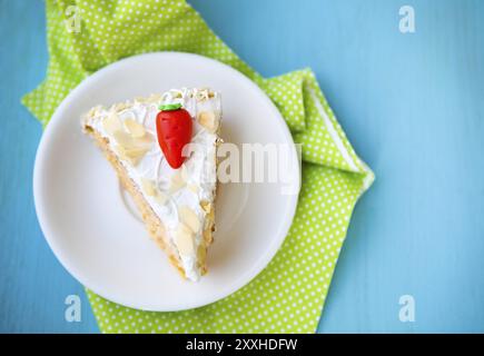Piece of carrot cake with icing and little carrot on blue wooden background Stock Photo