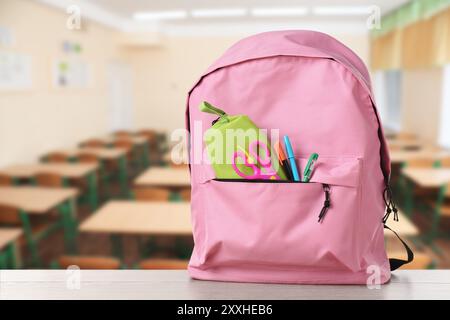 Pink backpack with stationery on school desk in classroom. Space for text Stock Photo