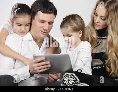Happy family of mother, father and daughters sitting on a sofa at home having fun using a tablet computer Stock Photo