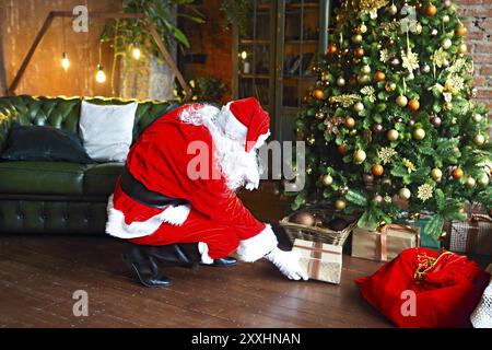 Santa Claus secretly putting gift boxes under the Christmas tree. Xmas Stock Photo
