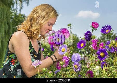 Young dutch redhead woman smelling summer flowers in garden Stock Photo