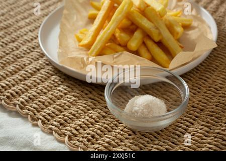 A view of a glass condiment cup of seasoned salt, next to a pile of French fries. Stock Photo