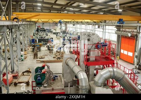 Wide-angle view of large manufacturing plant filled with various heavy machinery and equipment. Several workstations are visible with an overhead crane system installed Stock Photo