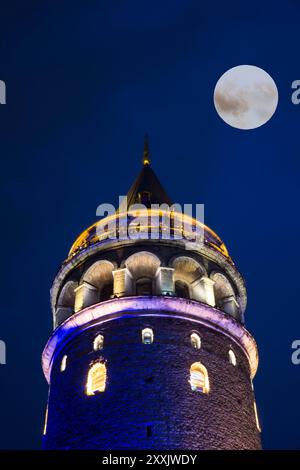 A vertical shot of the Galata Tower in Istanbul, Turkey, at night with the full moon Stock Photo