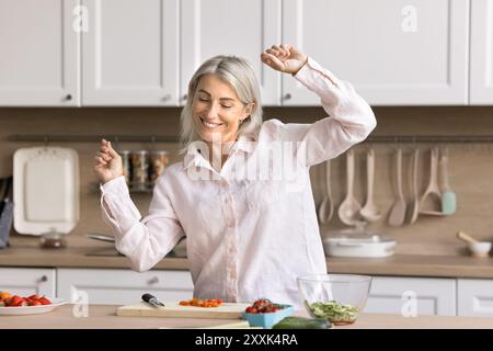 Happy mature woman dance and cook in the kitchen Stock Photo