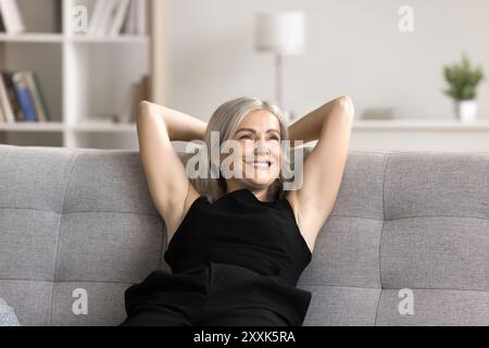 Smiling female leaned on cozy sofa with hands behind hands Stock Photo