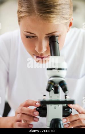 Taking closer look. Concentrated young female scientist using microscope while working in the laboratory Stock Photo