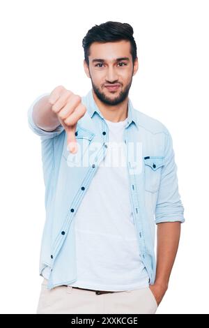 Too bad! Disappointed young Indian man showing his thumb down and making a face while standing against white background Stock Photo