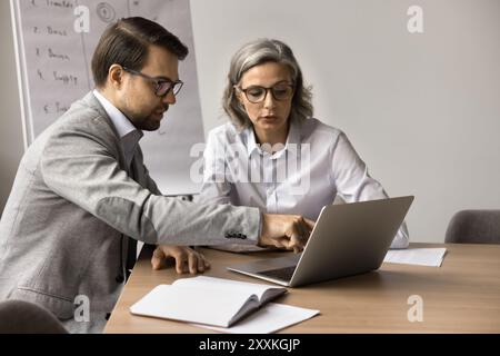 Two businesspeople sitting at table focused on laptop screen Stock Photo