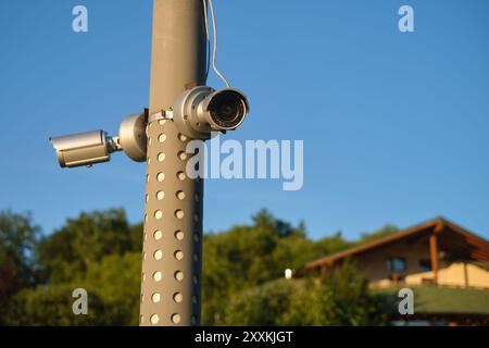 Two security cameras mounted on a pole with a house in the background under a clear blue sky. Outdoor security surveillance concept. Stock Photo