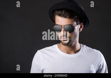 Confident and handsome. Handsome young man in sunglasses and fedora standing against black background Stock Photo