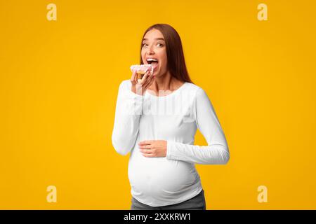 Pregnant Woman Eating Donut On Pink Background, Studio Shot Stock Photo