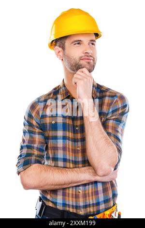 Thinking about new project. Thoughtful young male carpenter in hardhat holding hand on chin and looking away while standing against white background Stock Photo