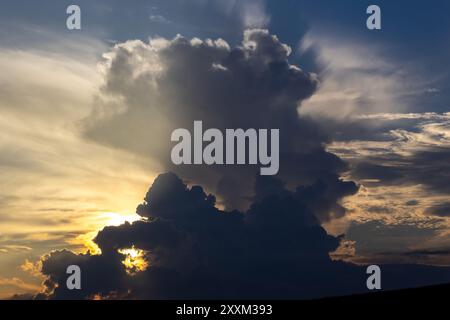 Amazing sky is filled with dark clouds, sunlight playing hide-and-seek behind them. Dramatic sky and dark black gray clouds as background. Stock Photo