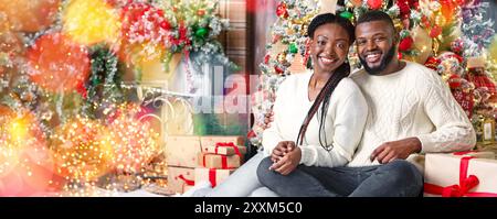 Black couple posing near Christmas tree, sitting on floor and smiling. Stock Photo