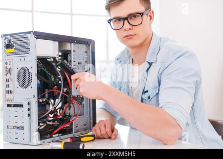 Master of computers.  Portrait of handsome young man repairing computer while sitting at his working place Stock Photo