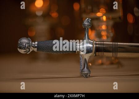 Silver medieva katana sword with rope pattern handle and ornate designs in gold protective sleeve on warm glow background Stock Photo