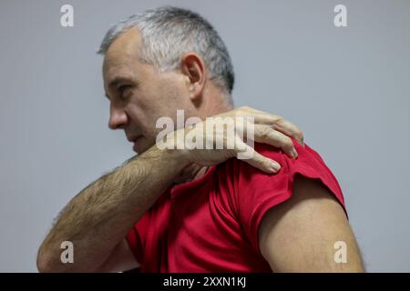 Mature man suffering from shoulder and back pain while sitting on chair and working from home. Stressed mature businessman suffering from neck pain an Stock Photo