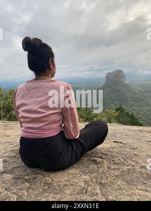 Woman sitting on Pidurangala Rock looking at Sigiriya, vertical photo Stock Photo